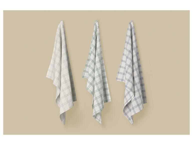 Trois torchons à carreaux beiges, verts et bleus suspendus à un mur.
