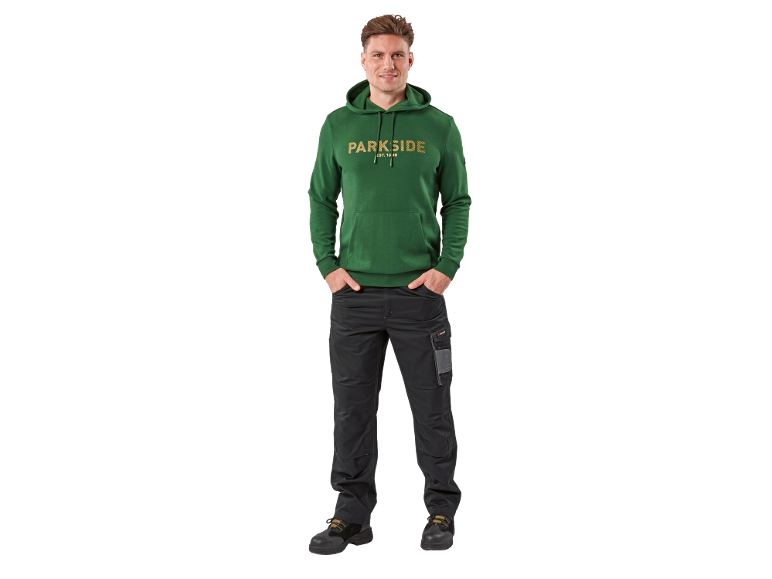 Homme en sweat à capuche vert avec texte et pantalon de travail noir.