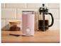 Moulin à café rose, cafetière à piston et café moulu sur un comptoir en bois.