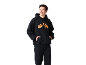 Homme souriant portant un sweat à capuche noir avec un motif orange et un pantalon de survêtement noir.