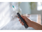 Une main tient une brosse à dents électrique noire avec une tête verte dans une salle de bain.