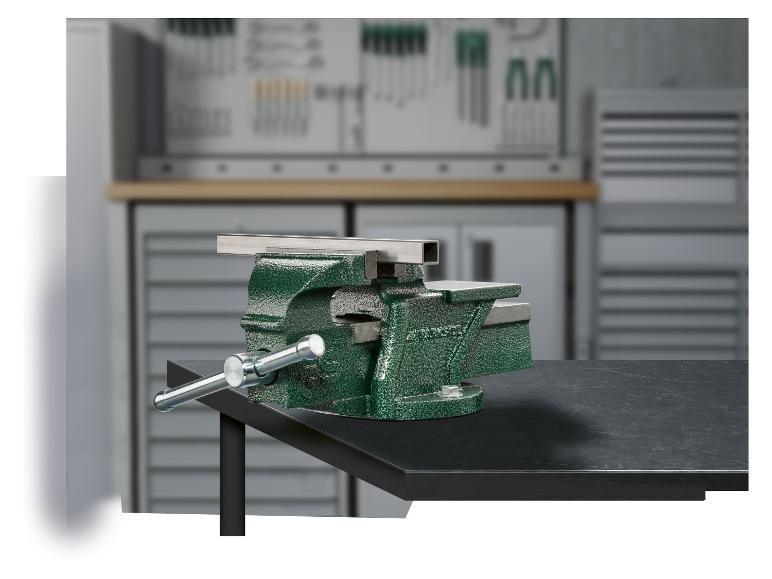Étau d'établi vert avec une pièce métallique serrée, sur un établi dans un atelier.