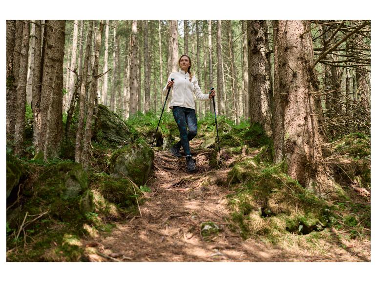Femme en veste et leggings, faisant de la randonnée avec des bâtons de trekking en forêt.