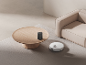 Robot aspirateur nettoyant le tapis à côté d'une table basse et d'un canapé.