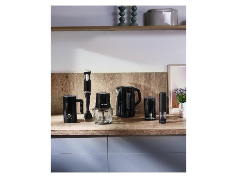 Bouilloire noire, mixeur plongeant, hachoir, mousseur à lait et moulin à épices sur un comptoir en bois.