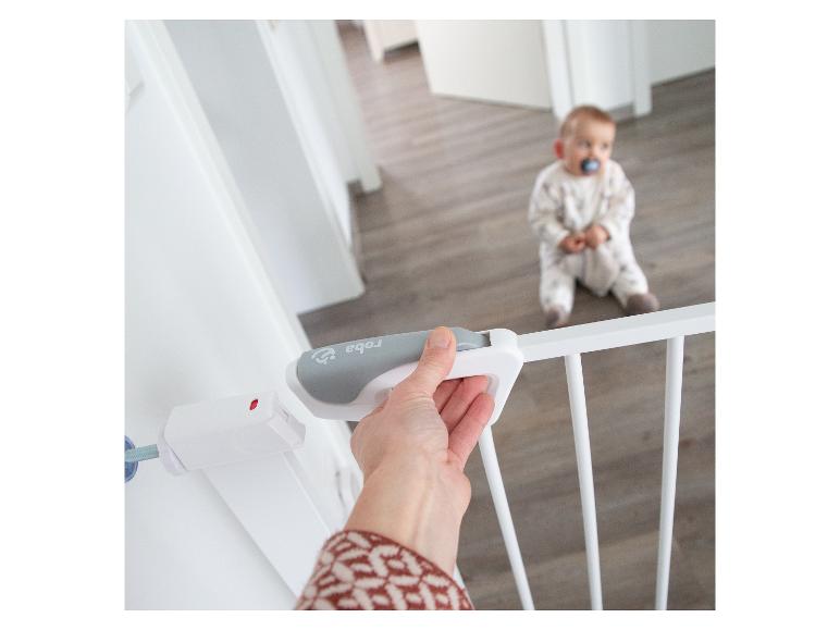 Main ouvrant une barrière de sécurité blanche avec un bébé en arrière-plan