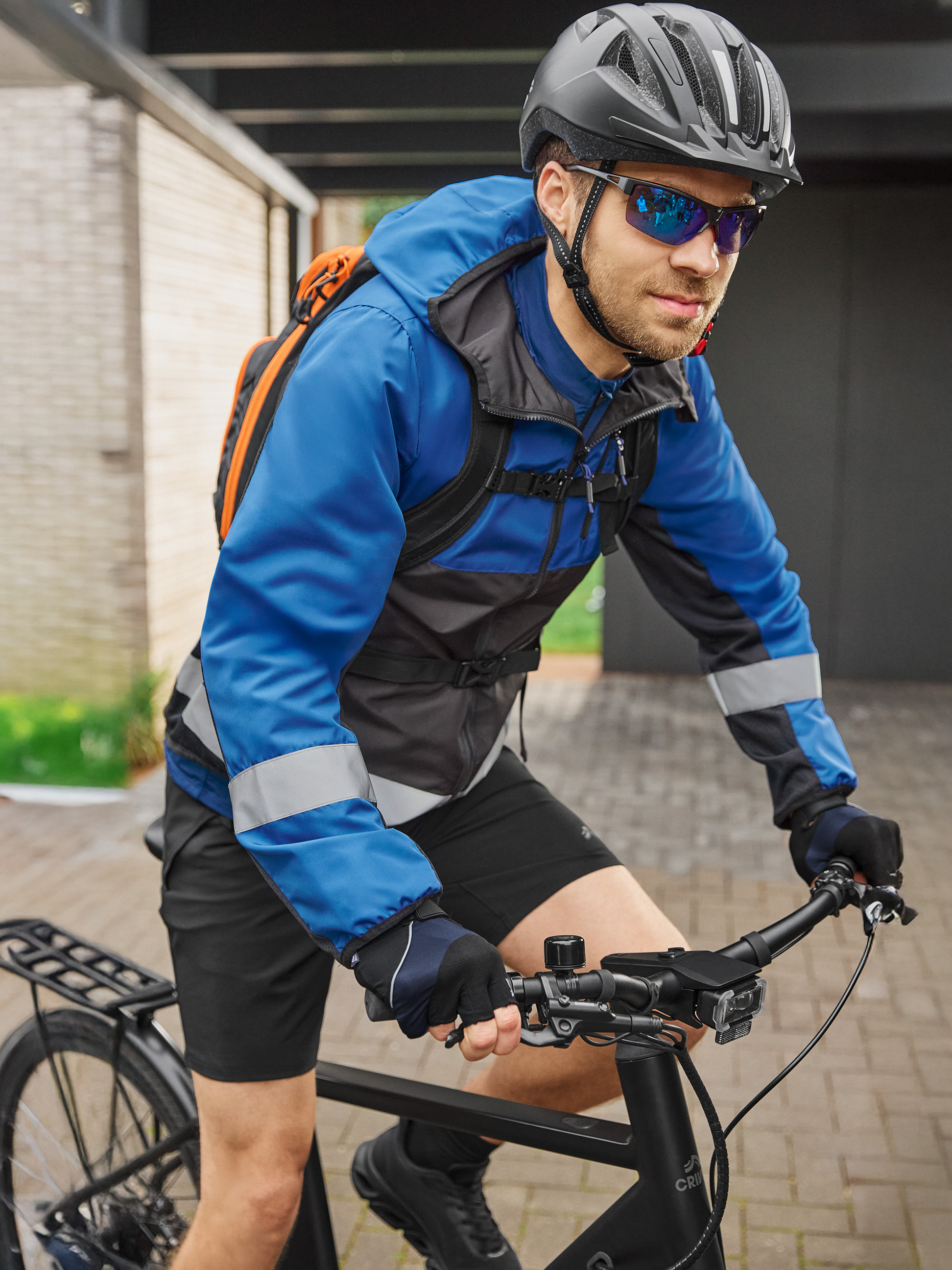 Cycliste en veste de cyclisme bleue et noire, casque et lunettes de soleil, sur un vélo noir.