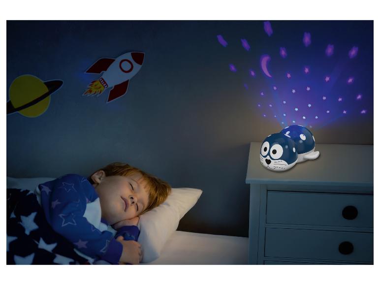 Un enfant dort dans un lit avec un projecteur de veilleuse en forme de phoque projetant des étoiles et des lunes.