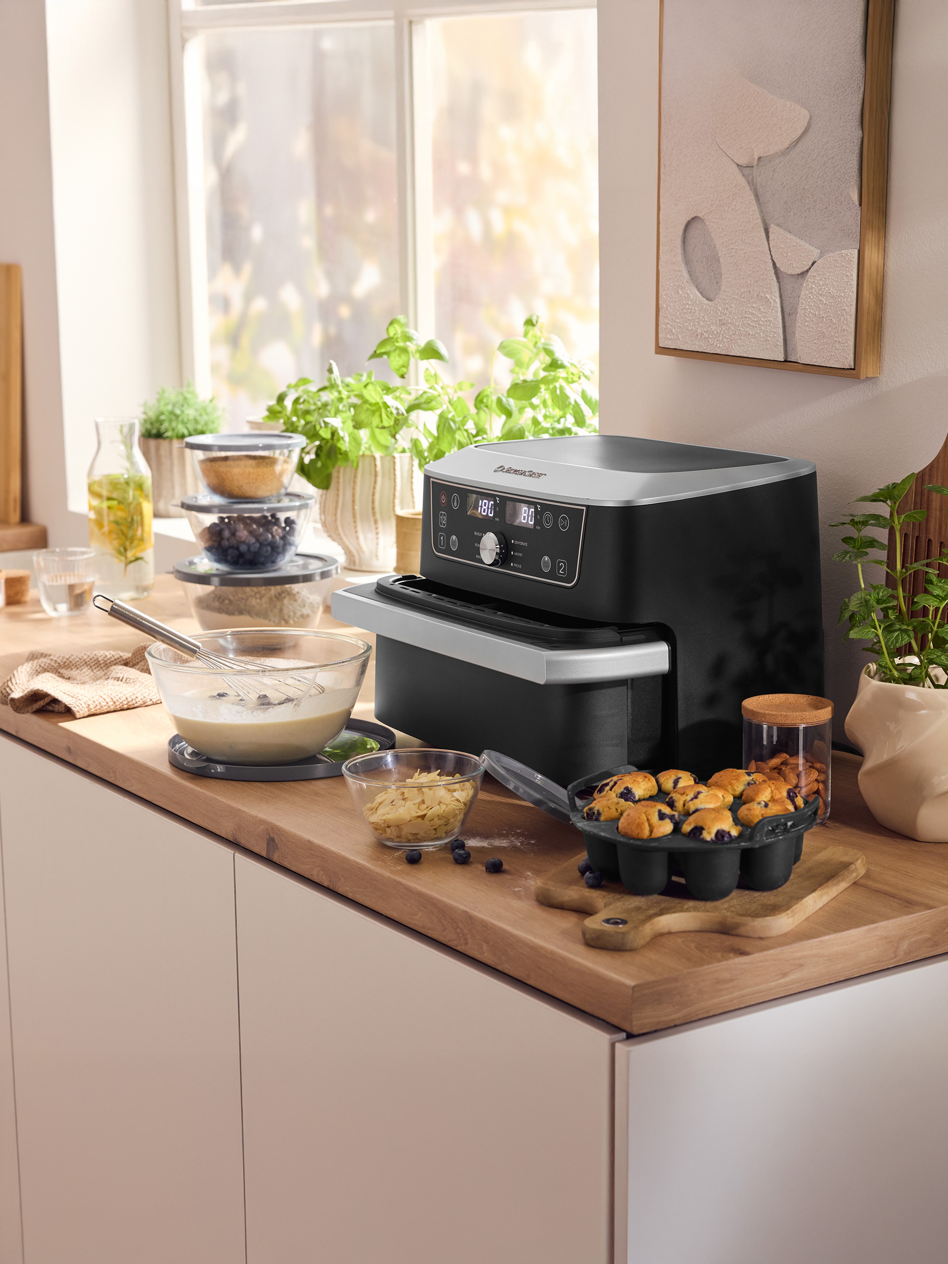 Comptoir de cuisine avec une friteuse à air Silvercrest, un moule à muffins avec des muffins aux myrtilles et des ingrédients de cuisson.