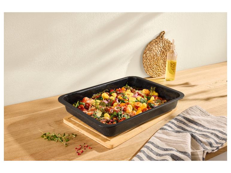 Plat de cuisson rempli de gnocchis, tomates, épinards et herbes sur une table en bois.