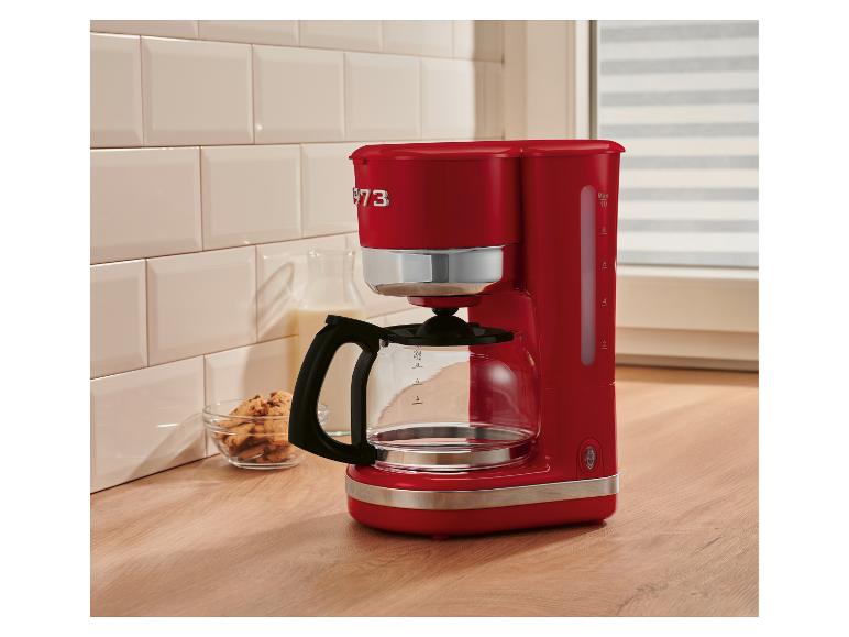 Cafetière rouge sur un comptoir de cuisine, avec des biscuits et du lait en arrière-plan.