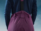 Une femme porte un pull bleu marine et un pantalon violet avec des bretelles.