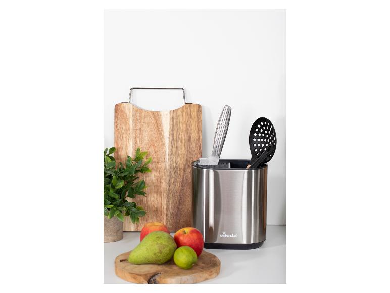 Support d'ustensiles de cuisine en acier inoxydable avec planche à découper et fruits sur un comptoir.