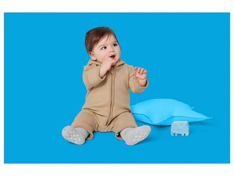 Adorables tout-petits en combinaison beige assis à côté d'un oreiller bleu et d'un jouet en bois.