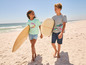 Deux enfants marchant sur la plage avec des planches de surf.