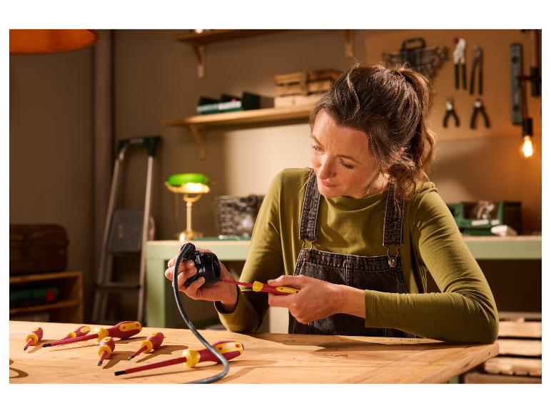 Femme utilisant un tournevis Parkside pour réparer un appareil électrique sur un établi en bois.