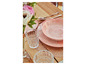 Une assiette rose et des verres sur une table en bois avec un dessous de verre rose.