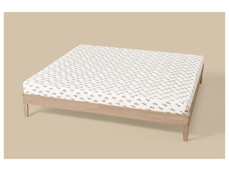 Cadre de lit avec matelas et drap-housse blanc à motif de feuilles brun-rouge.