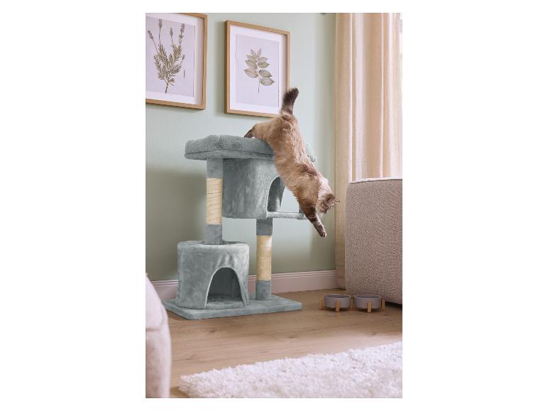 Chat sautant d'un arbre à chat multi-niveaux dans un salon avec des gamelles.