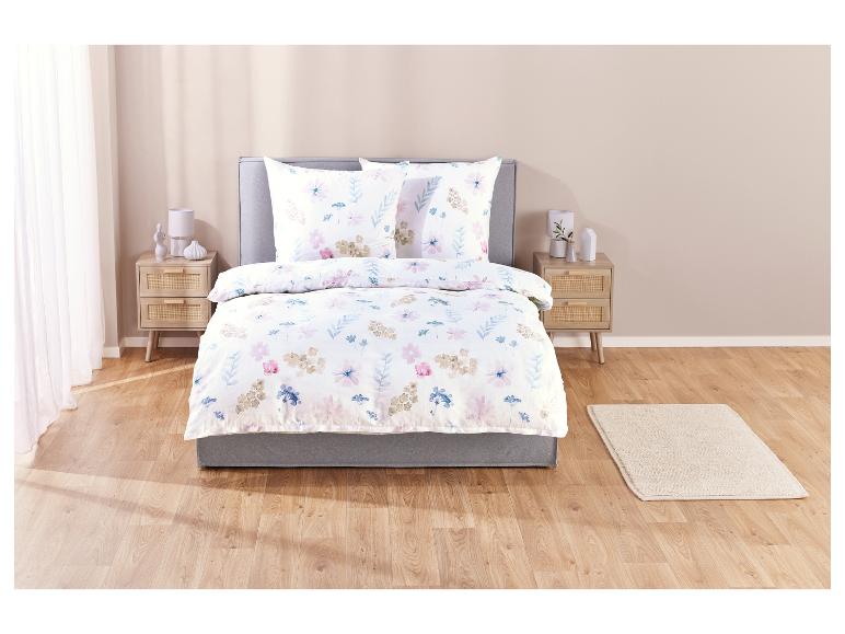 Une couette blanche à imprimé floral sur un lit avec une tête de lit grise.
