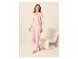 Femme en pyjama rose clair avec un cardigan et un pantalon, debout à côté d'une chaise.