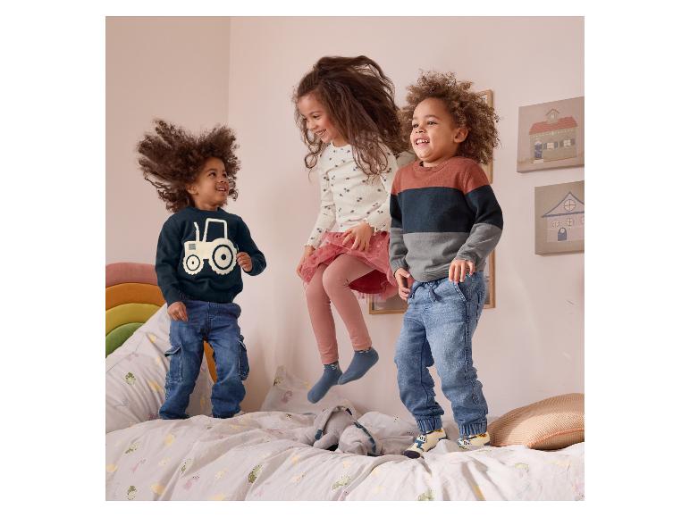Trois enfants sautent sur un lit avec de la literie pour enfants, vêtus de pulls et de chaussettes amusants.