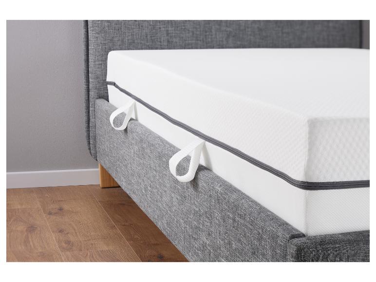 Un lit gris avec un matelas et des pieds en bois.