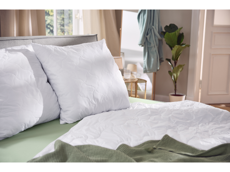 Oreillers et couette matelassés blancs sur un lit avec des draps et une couverture verts.