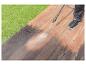 Une personne nettoie une terrasse en bois avec un nettoyeur haute pression.