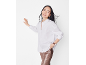 Femme en chemise blanche et pantalon brillant, souriante, appuyée contre un mur.