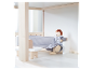 Poupée en bois assise sur un canapé gris dans une maison de poupées.
