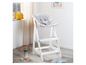 Une chaise haute blanche avec un coussin gris, un arc-en-ciel et une pile de jouets.