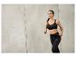 Une femme en soutien-gorge de sport noir et leggings de la marque Gymshark, en train de courir.