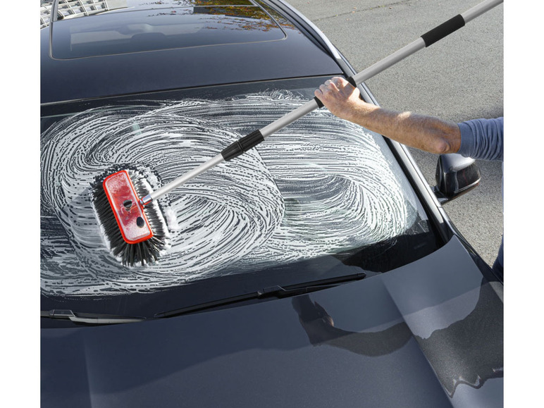 Un homme lave le pare-brise d'une voiture avec une brosse sur une perche télescopique.