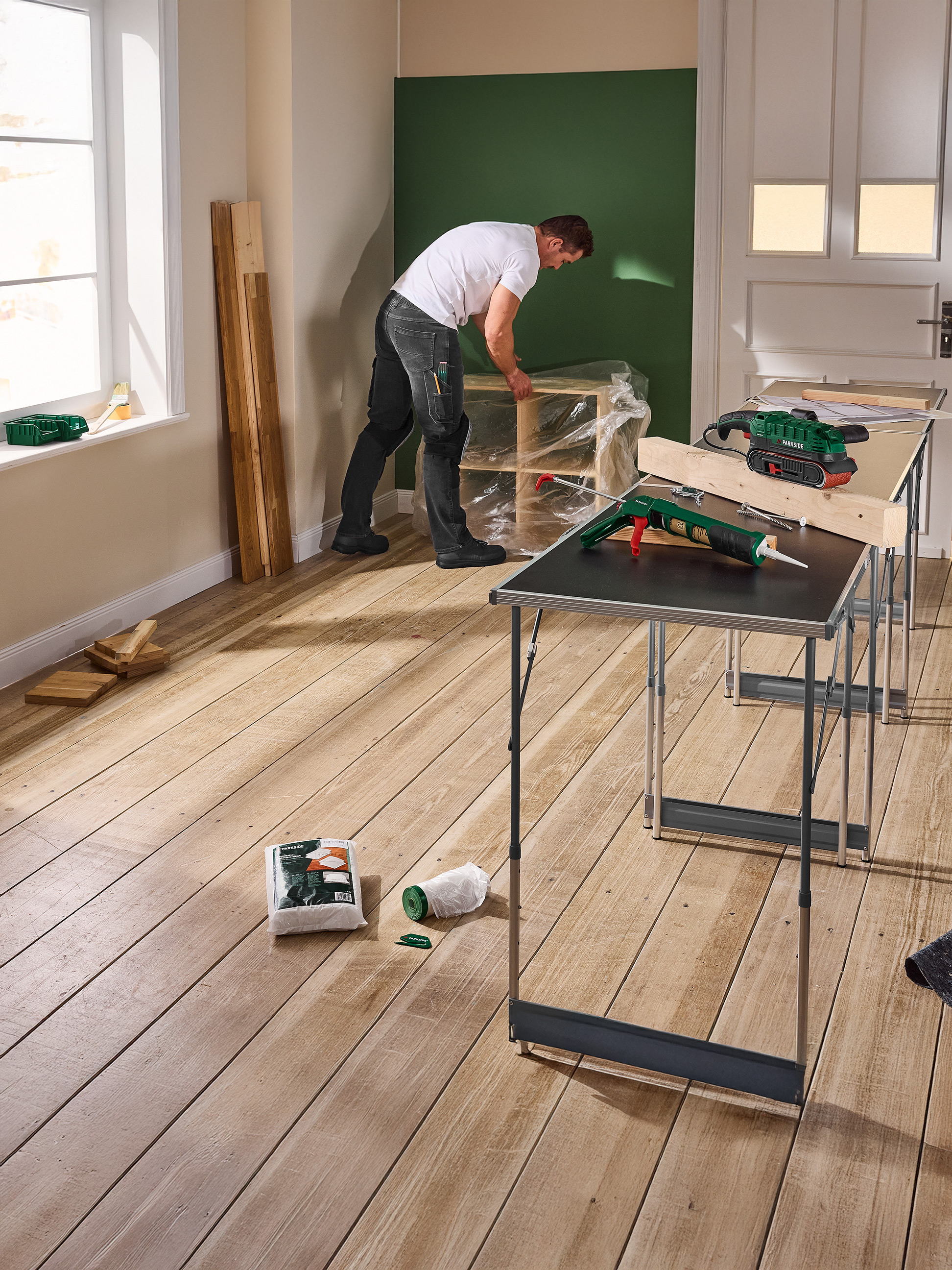 Homme travaillant sur un projet de bricolage avec des outils Parkside, dont une ponceuse et un pistolet à mastic, sur des tables pliantes.