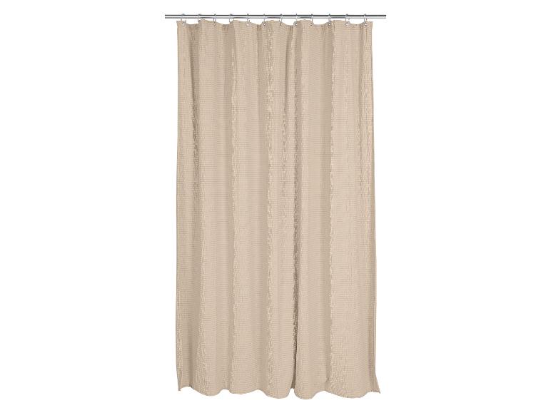 Rideau de douche beige avec un motif gaufré texturé, suspendu à une tringle argentée.