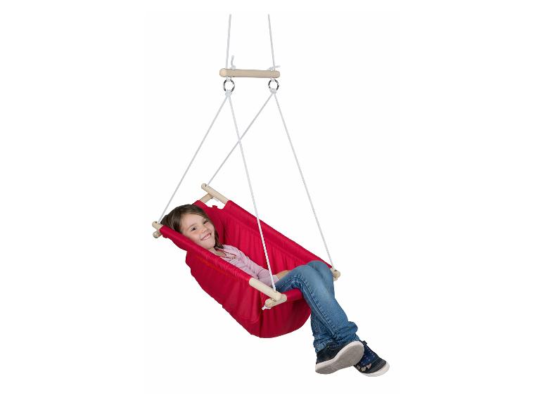 Une petite fille souriante se balance dans une balançoire en tissu rouge