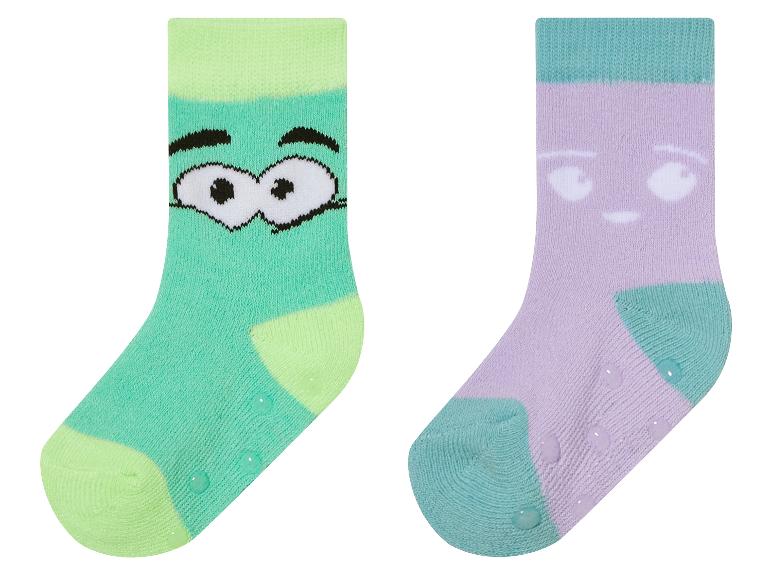 Deux paires de chaussettes pour bébé antidérapantes, une avec un visage de monstre vert et l'autre avec un visage violet.