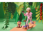 Fille avec un casque sur une trottinette, à côté d'un chien en peluche, dans un décor de jungle.