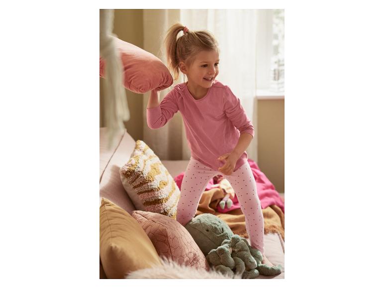 Une petite fille joue avec un oreiller et des peluches sur le canapé.