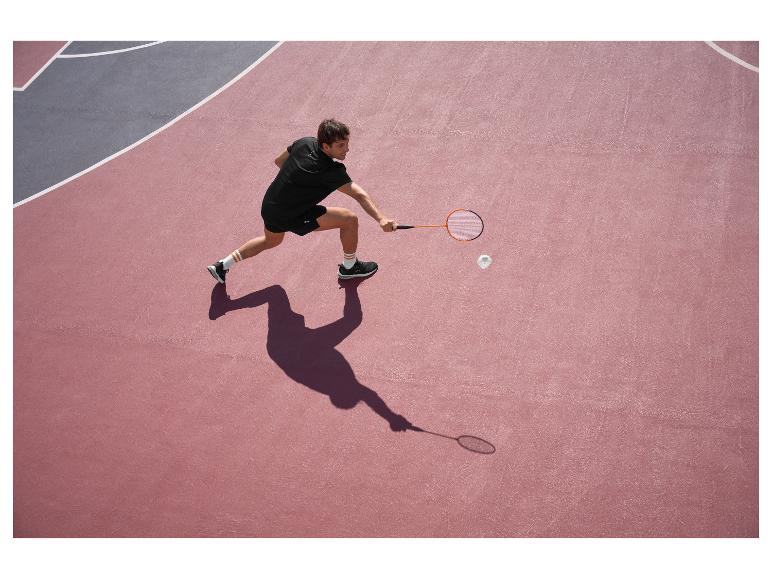 Homme en noir jouant au badminton sur un terrain rose et gris.