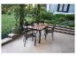 Table de jardin en bois avec quatre chaises sur une terrasse donnant sur un jardin.