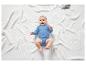 Un bébé dans un body bleu, allongé sur une couverture blanche.