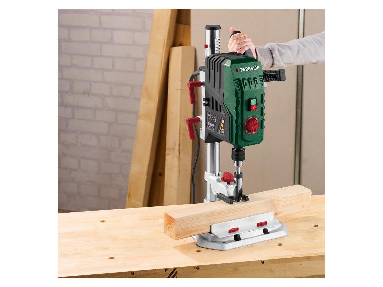 Personne utilisant un support de perceuse Parkside pour percer une poutre en bois sur un établi.