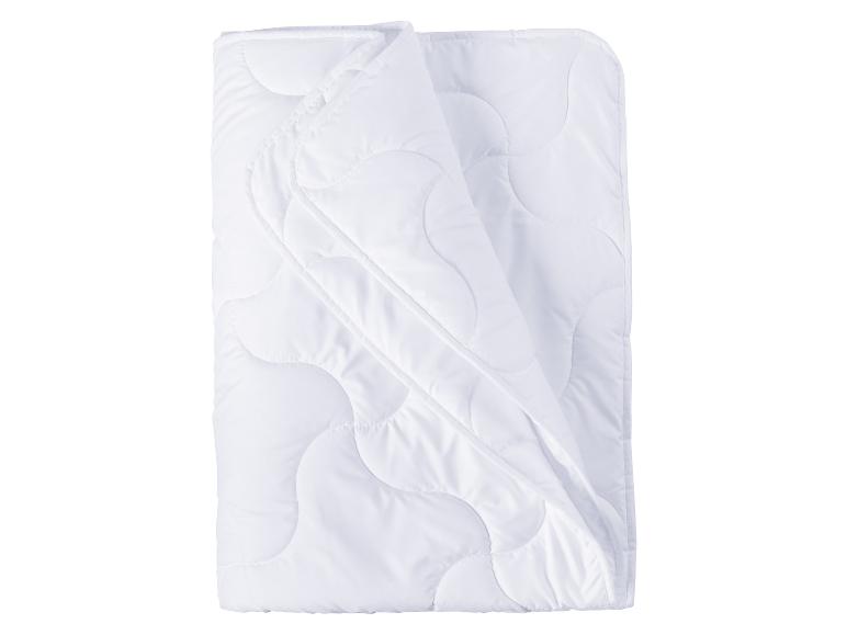 Couverture blanche matelassée, pliée sur un fond blanc.