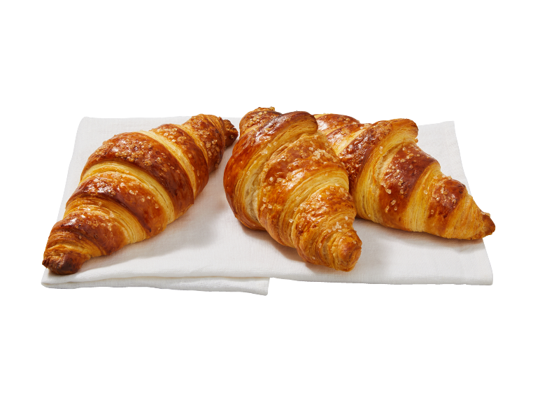 Trois croissants dorés aux cristaux de sucre sur une serviette blanche.