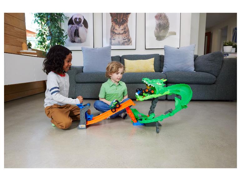 Deux garçons jouent avec un circuit de monster trucks avec un dragon vert.