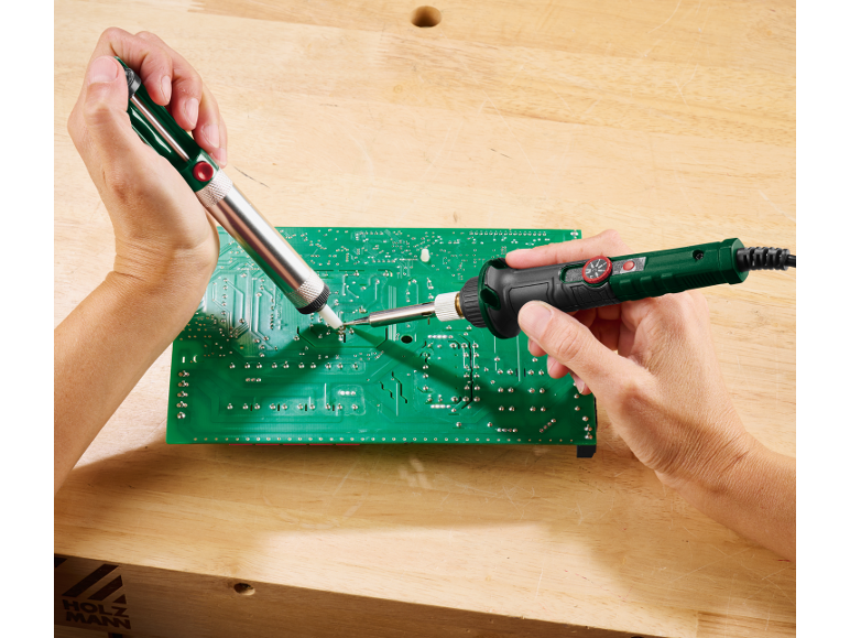 Mains soudant une carte de circuit imprimé avec un fer à souder et une pompe à dessouder
