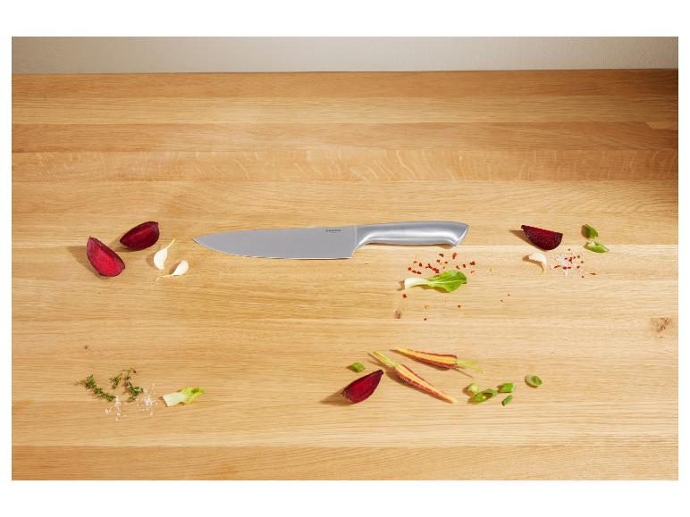 Couteau de chef sur une planche en bois avec légumes et épices.