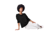 Modèle avec de grands cheveux afro pose avec un pull noir et un pantalon blanc.